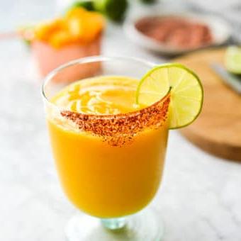 Ein Glas Frozen Mango Margarita mit Chilischnee-Rand, Zutaten für Mango Margaritas im Hintergrund
