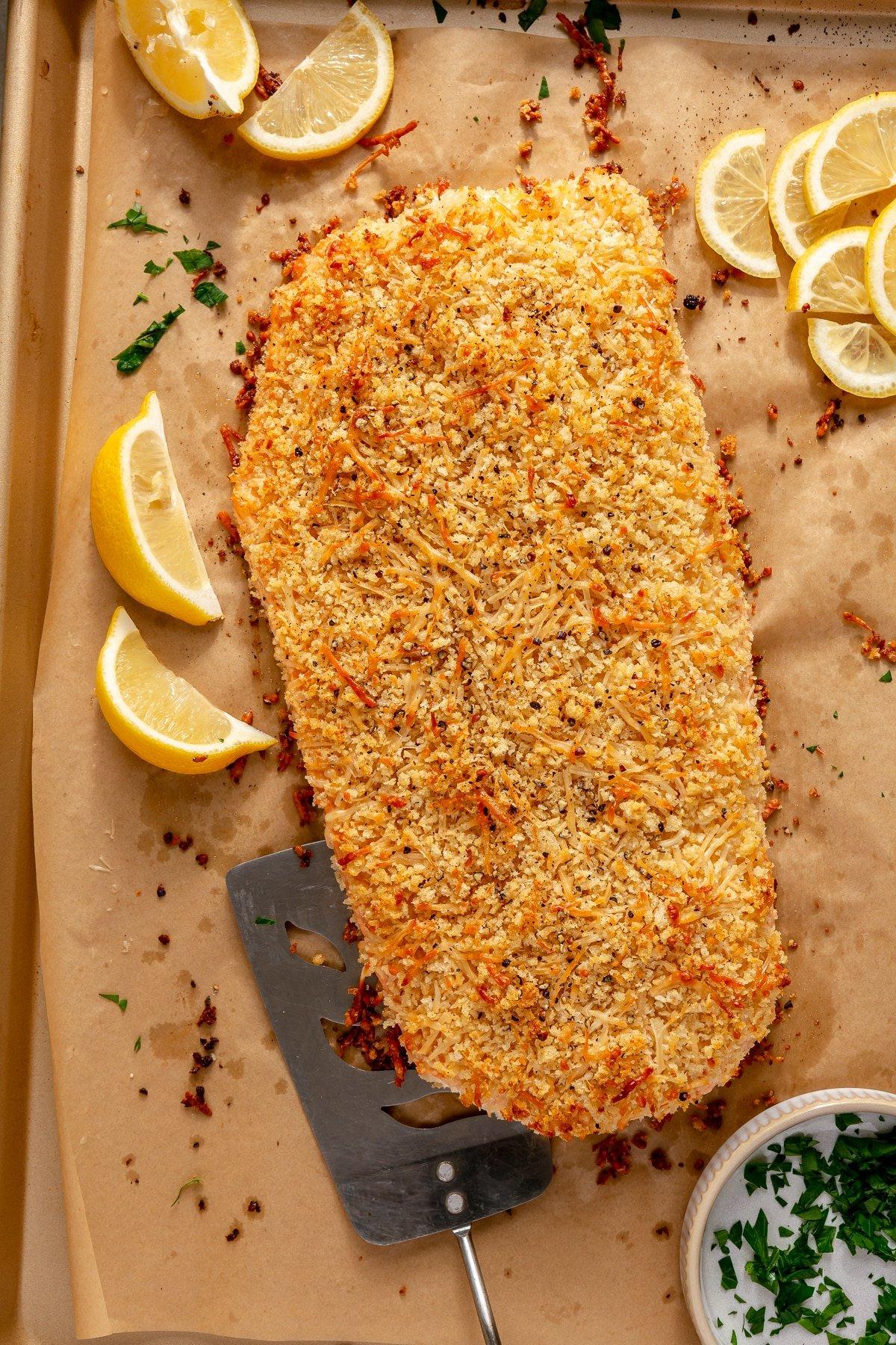 Ein Teller mit dem fertigen gebackenen Parmesan-Lachs, garniert mit Zitrone und Petersilie.