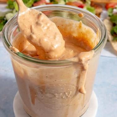 Ein Glas Burgersauce, aus dem jemand mit einem Löffel etwas Sauce schöpft.