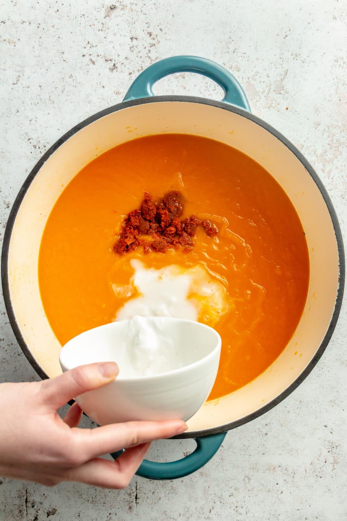 Eine Person gibt Kokosmilch in einen Topf mit Karottensuppe.
