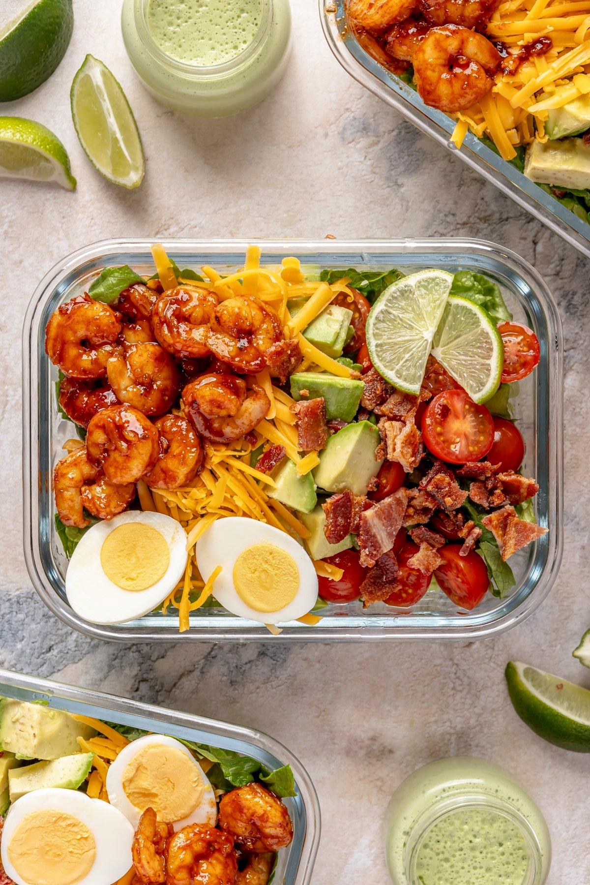 Ein Glas-Meal-Prep-Behälter gefüllt mit scharfem Garnelen-Cobb-Salat.