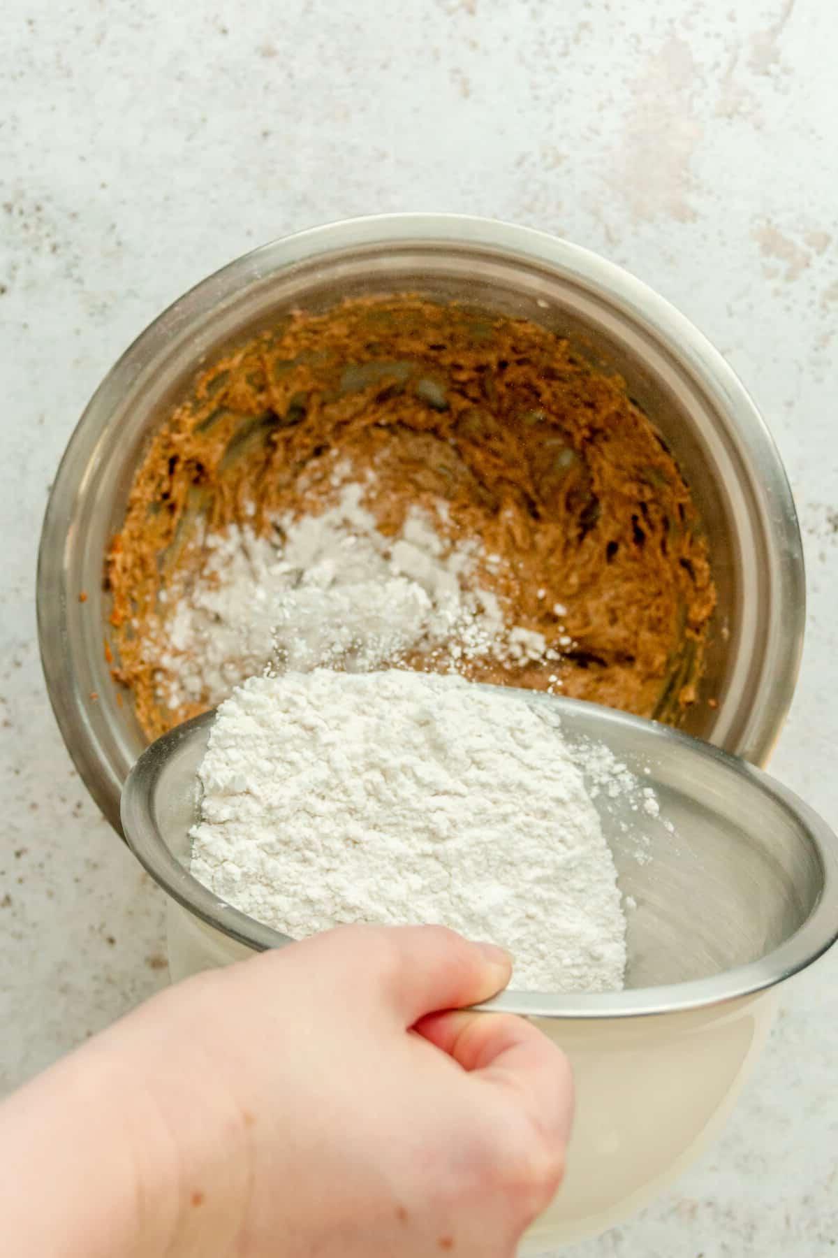 Trockene Mischung wird über die Butter-Zucker-Kürbispüree-Mischung in einer Edelstahlschüssel auf hellem Untergrund gerührt.