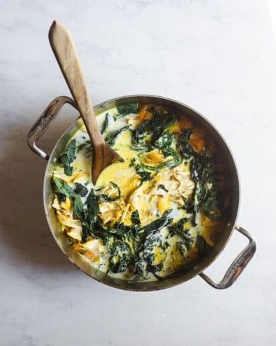 Ein großer Topf mit heilender Kurkuma-Hühnersuppe und einem Holzlöffel darin