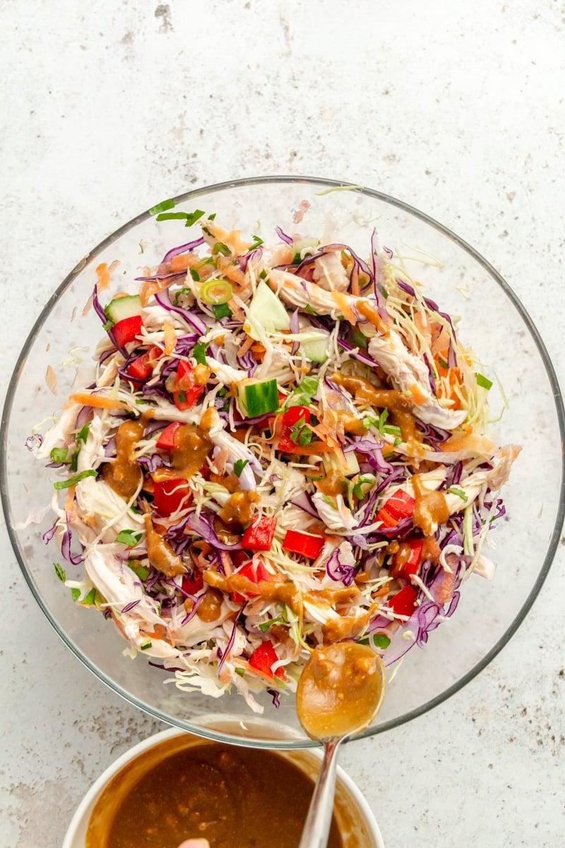 Thai-inspirierter Hähnchensalat in einer großen Glasschüssel. Eine braune Sauce wird darüber geträufelt.