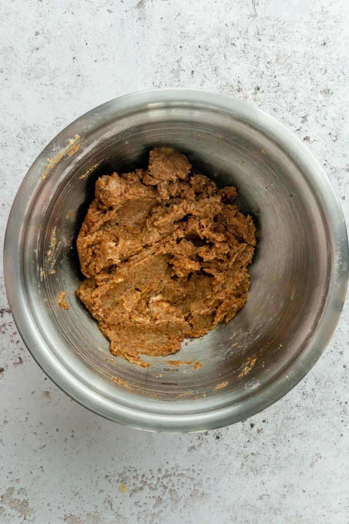 A crumble mixture sits in a stainless steel bowl on a light gray surface.