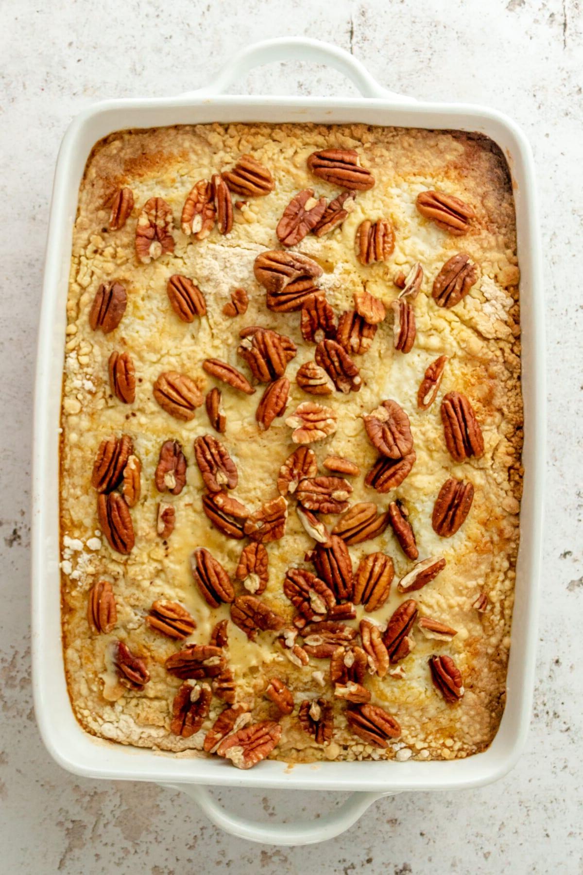 Pekannüsse liegen auf einem Kürbis-Dump-Cake in einer weißen, rechteckigen Auflaufform auf hellgrauem Untergrund.