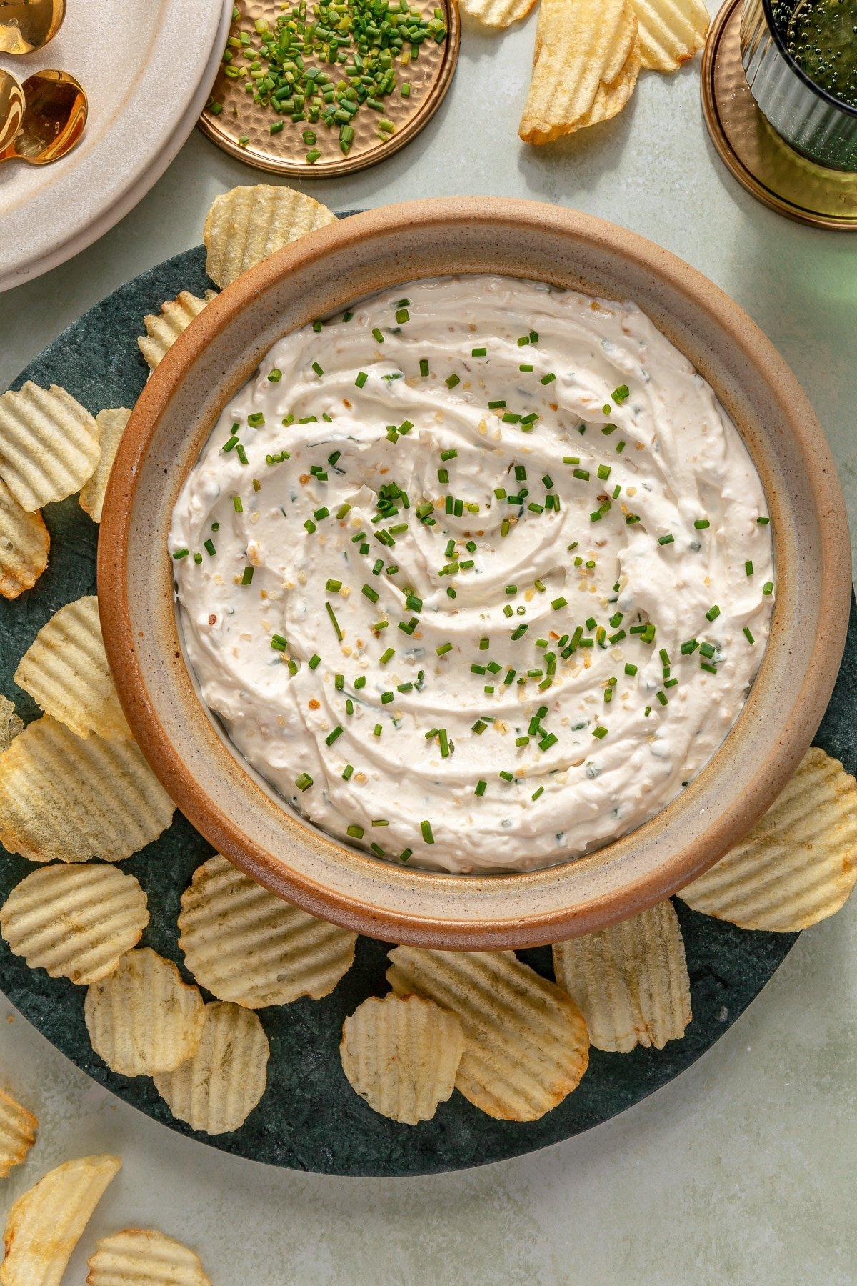 Eine große Schüssel Französischer Zwiebeldip, garniert mit frischem Schnittlauch und umgeben von Kartoffelchips.
