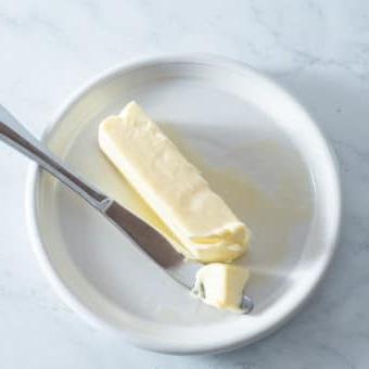 Ein Stück weiche Butter auf einem kleinen weißen Teller mit einem Buttermesser daneben