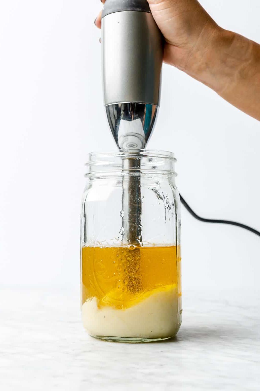 Hand, die einen Stabmixer in einem großen Einmachglas hält, während sich am Boden Mayonnaise bildet und Öl oben aufliegt.
