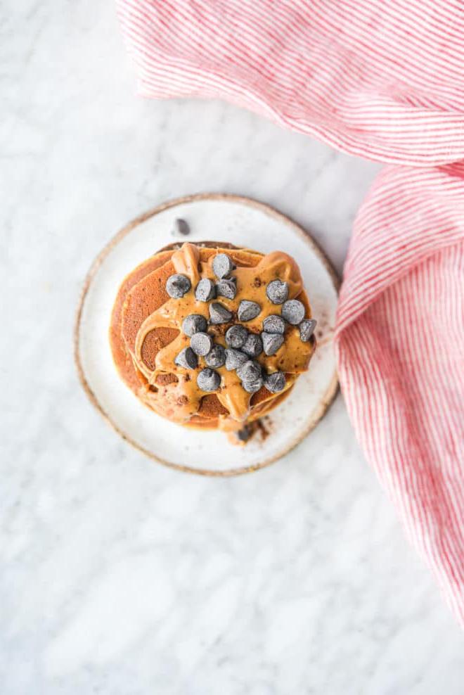 Eine Draufsicht auf einen Stapel Protein-Pancakes, garniert mit Erdnussbutter und Schokoladenstückchen.