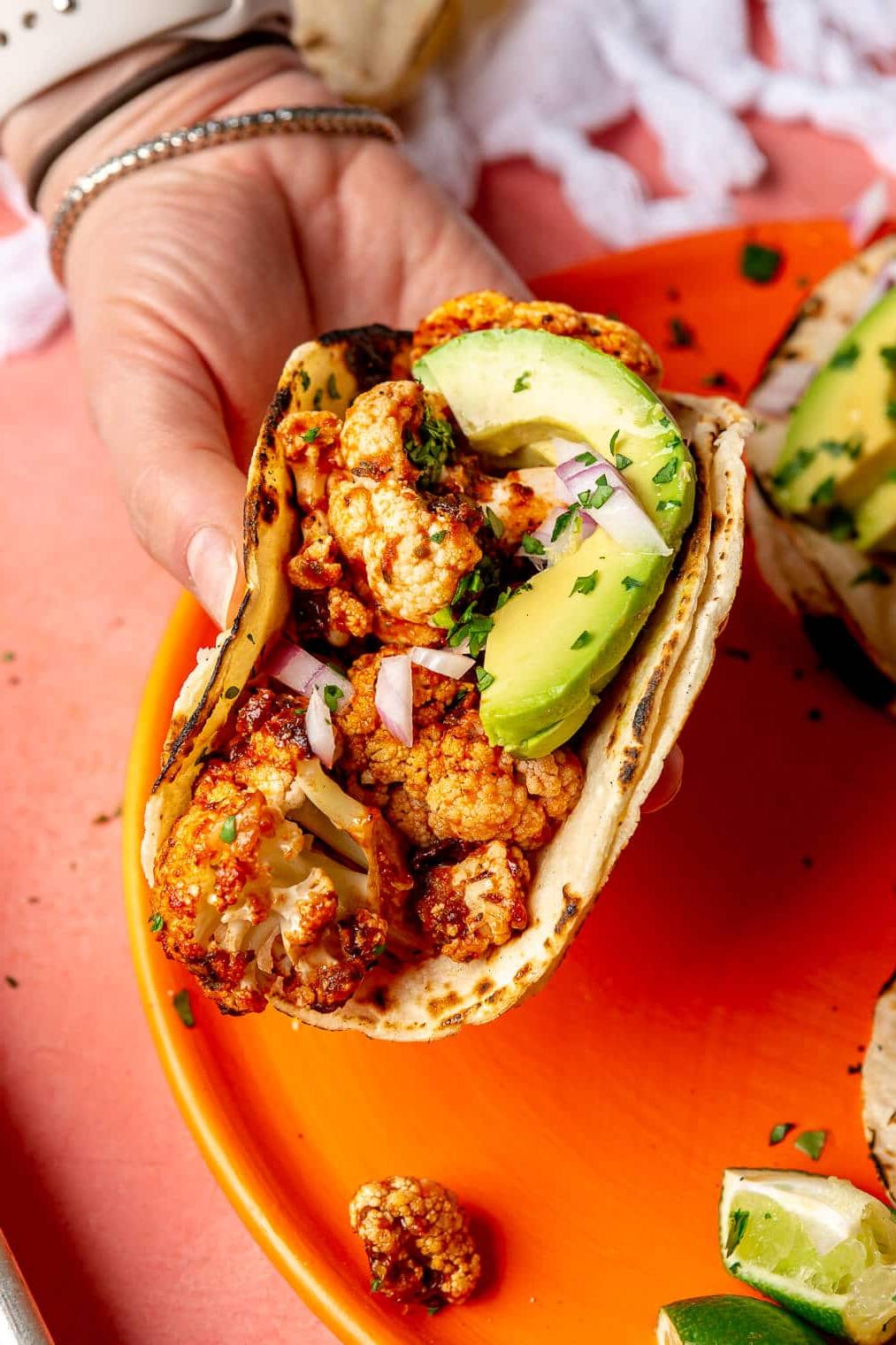 Eine Person, die einen Blumenkohl-Tinga-Taco hält.