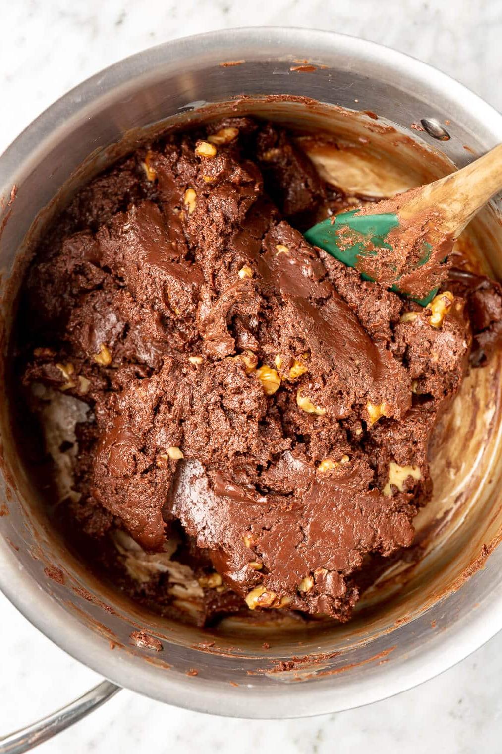 220907_Dark Chocolate Walnut Fudge-08 Spatel rührt geschmolzene Schokolade, Kondensmilch und Walnüsse in einem Edelstahltopf um.