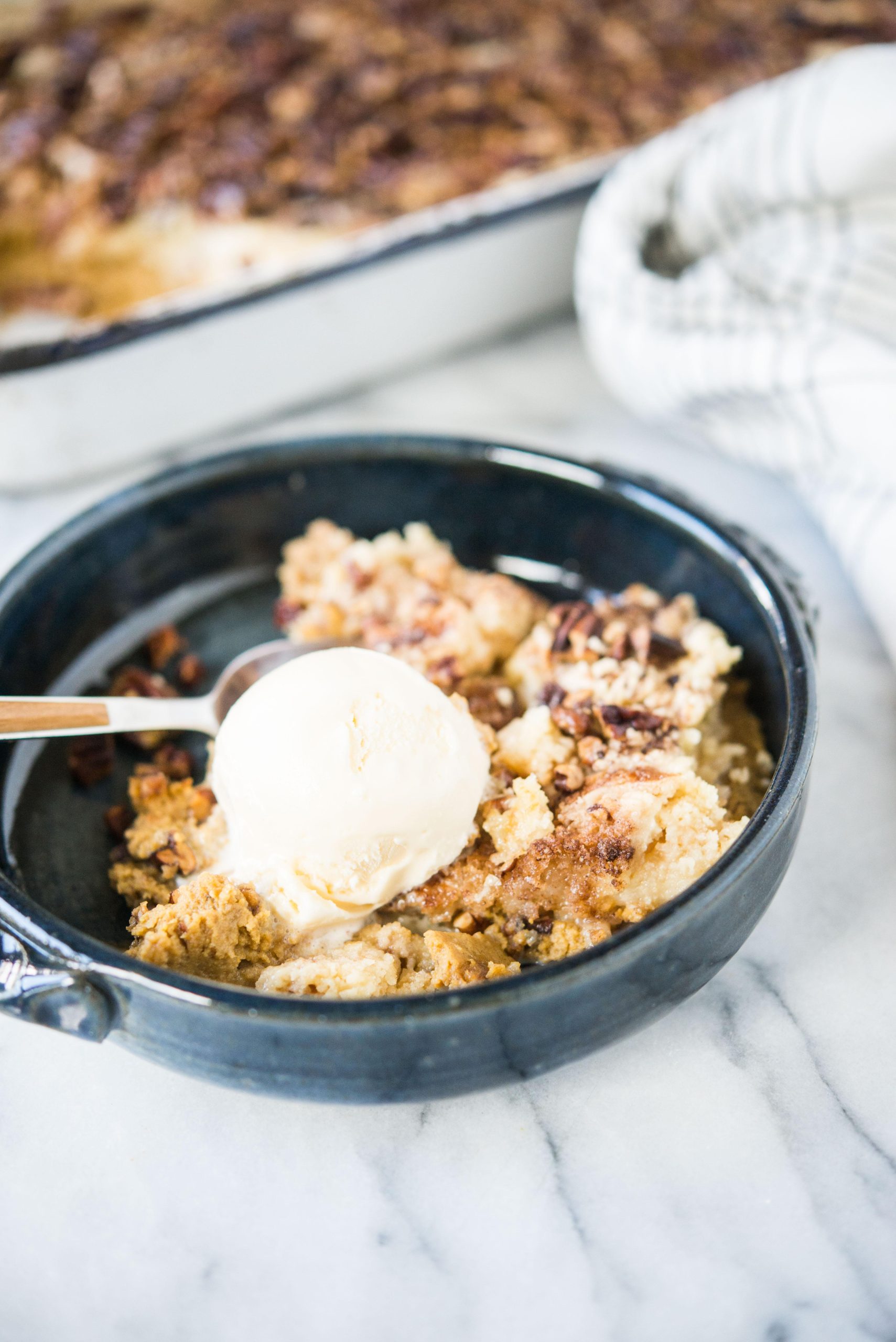 Dunkelblaue Schüssel mit Kürbis-Dump-Cake und einer Kugel Eiscreme darauf.