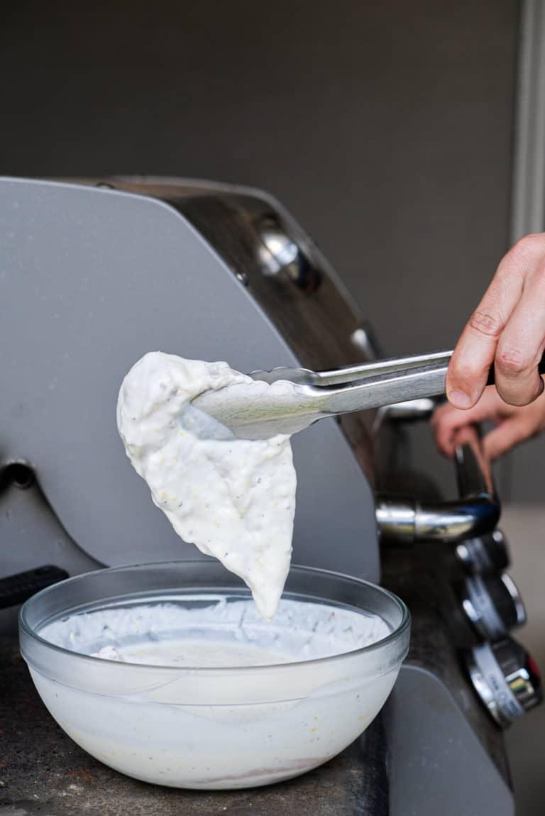 In Zitronen-Joghurt marinierte Hähnchenbrust wird mit einer Zange gehalten und ist bereit für den Grill