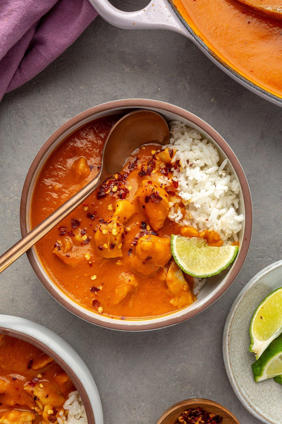 Einfaches Kürbiscurry-Rezept 8 Eine Servierschüssel mit Reis ist mit Kürbis-Curry belegt. Ein Kupferspoon steckt in der Schüssel zusammen mit einer Limettenscheibe.