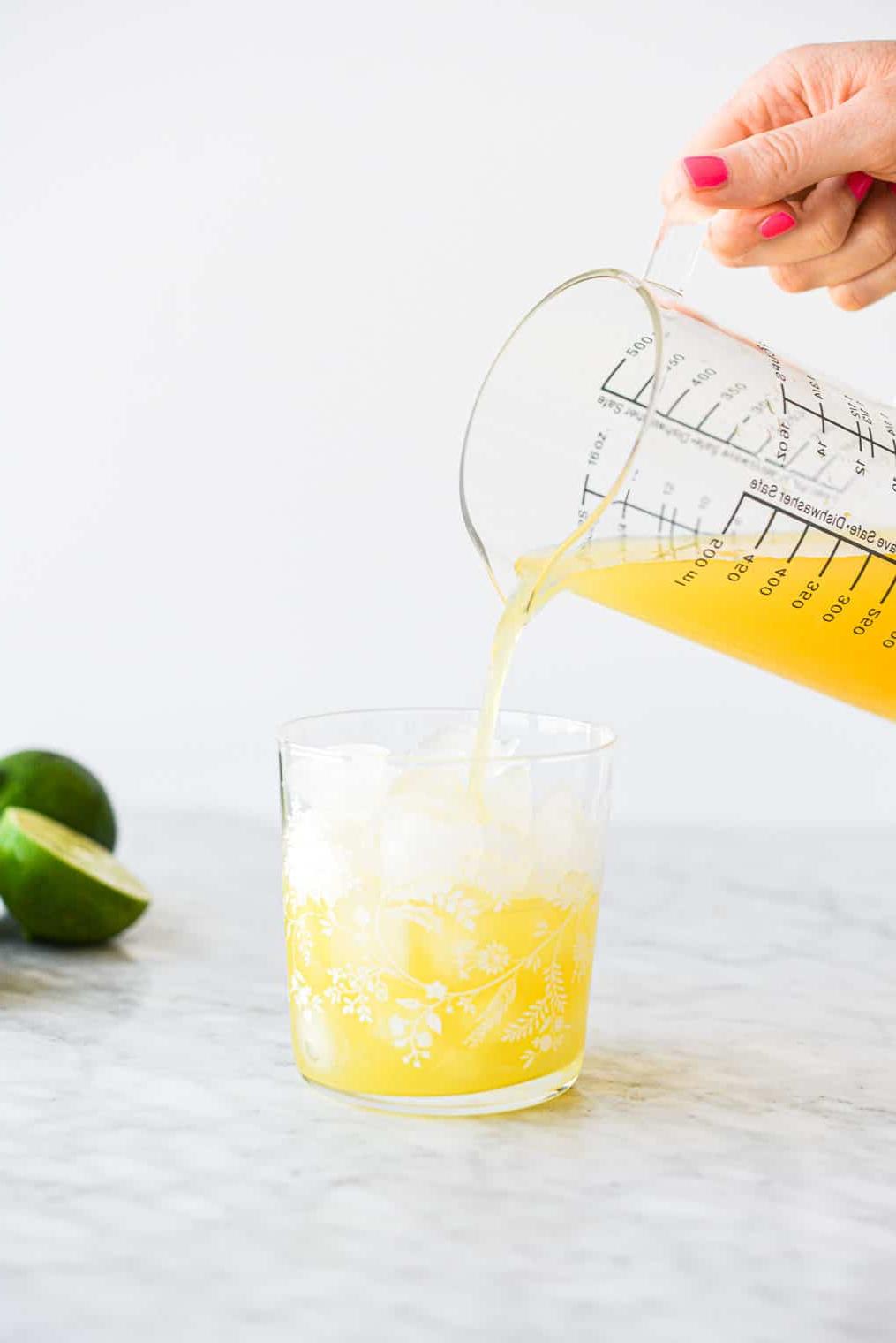 Eine Person gießt ein Ananas Margarita aus einem großen Messbecher in ein mit Eis gefülltes Margarita-Glas.