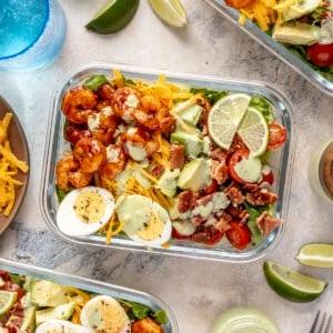 Ein Glas-Meal-Prep-Behälter gefüllt mit scharfem Garnelen-Cobb-Salat.