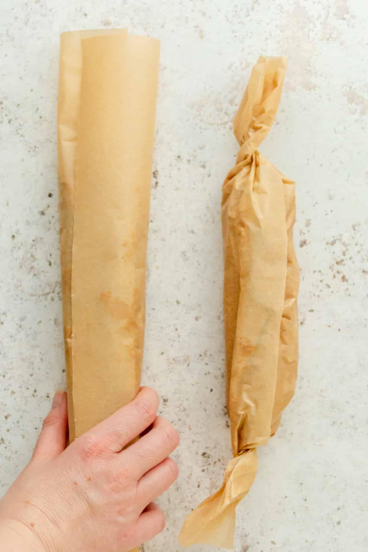 In Backpapier gewickelter Keksteig wird auf einer grauen Oberfläche gerollt.