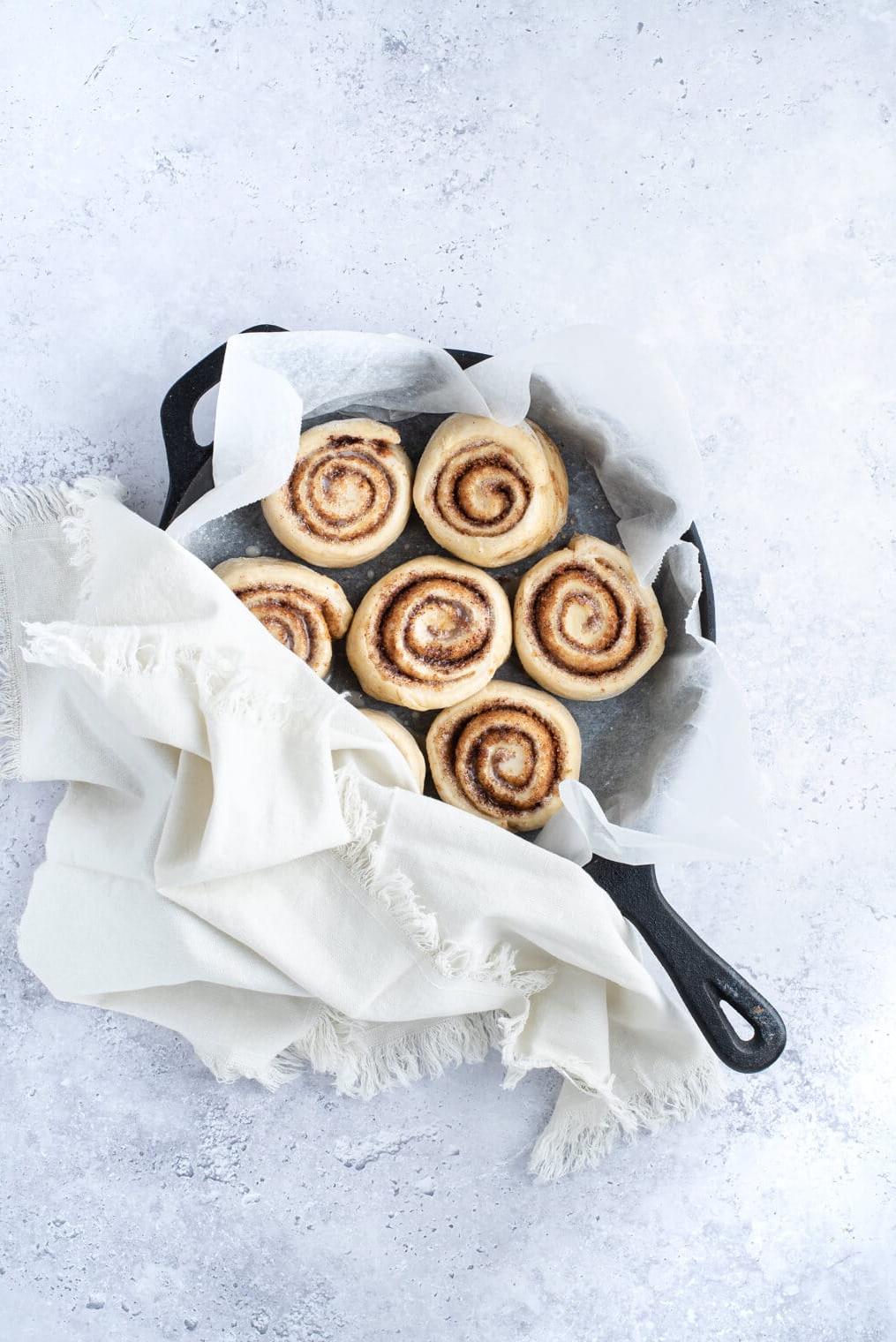 Eine Pfanne mit veganen Zimtschnecken, bedeckt mit einem Küchentuch, vor dem zweiten Gehen