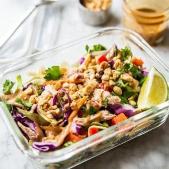 Ein farbenfroher Thai-Hähnchensalat in einem einzelnen Glas-Meal-Prep-Behälter mit Erdnussdressing und zerstoßenen Erdnüssen im Hintergrund