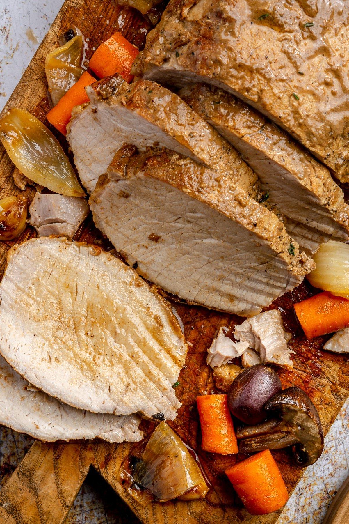 Der Schweinebraten wurde in Scheiben geschnitten und liegt auf einem braunen Schneidebrett.
